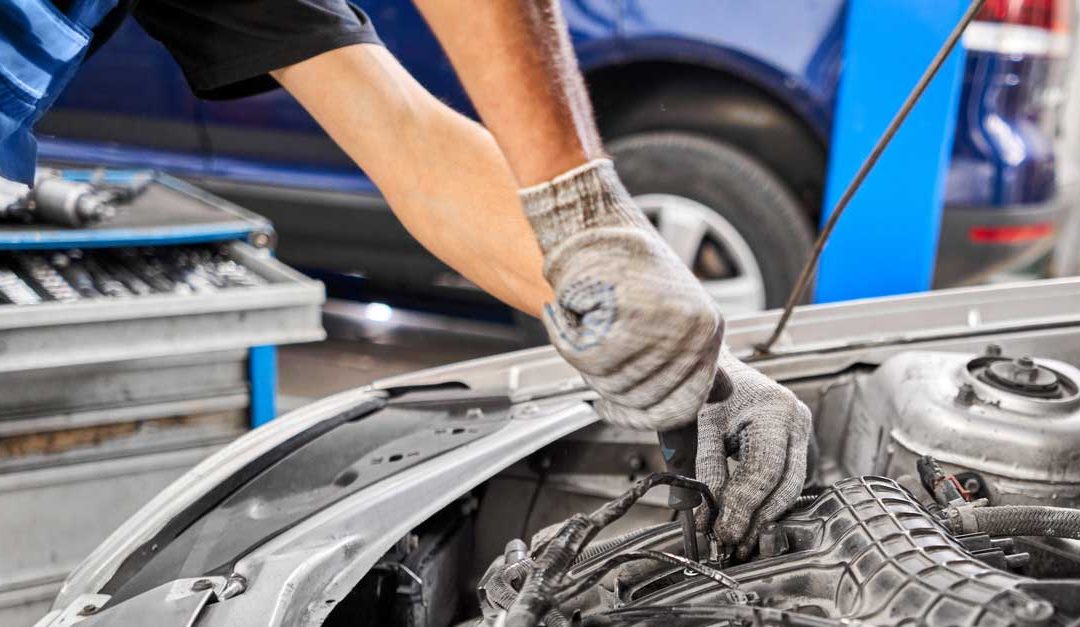 A mechanics hands working on a car with the hood up